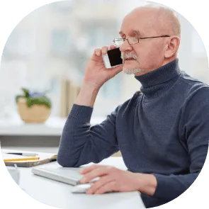 Un homme âgé à lunettes, au téléphone, assis à son bureau près de la fenêtre