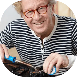 Un homme aux lunettes rouges répare une pièce mécanique avec un outil bleu