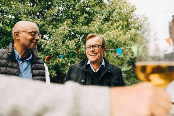 Deux hommes retraités souriants discutent en extérieur, dans un jardin