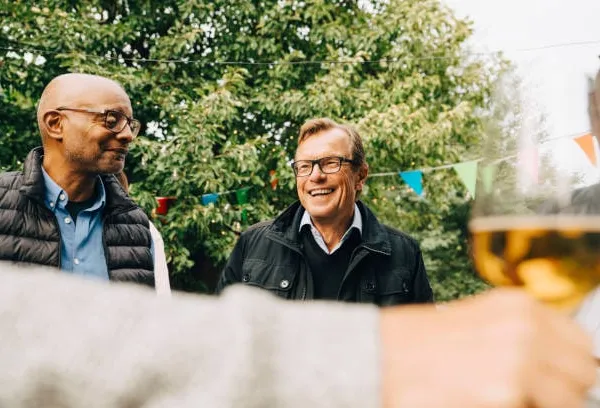 Deux hommes retraités souriants discutent en extérieur, dans un jardin