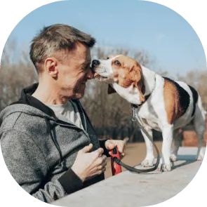 Un homme souriant se fait lécher le visage par un chien beagle tenu en laisse, en extérieur