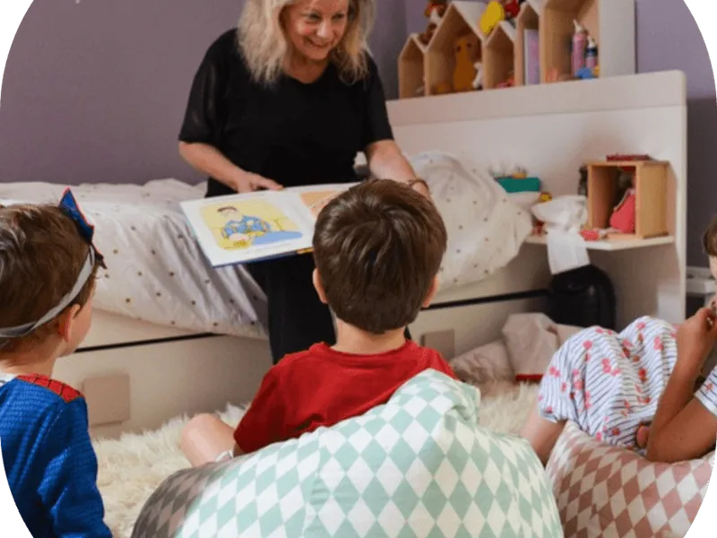 Une femme lit un album illustré à un groupe de jeunes enfants assis sur des coussins
