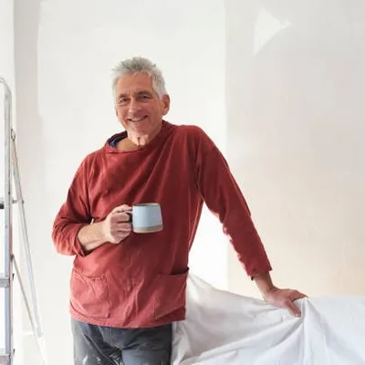Fred, en pull rouge, près d'un escabeau dans une pièce en cours de travaux