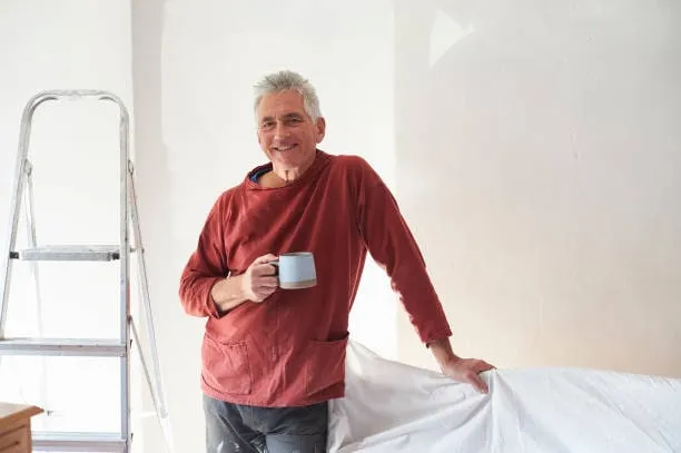 Un homme en pull rouge, près d’un escabeau, dans une pièce en cours de travaux