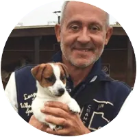 Portrait de Frédéric, cheveux gris, polo sombre, tenant un jeune chien dans ses bras