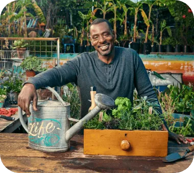Un homme souriant arrose un potager surélevé en bois avec un arrosoir métallique